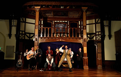 Production photo by Will Kirk Photography of members of the cast peforming a song, with guitar, saxaphone, a box for a drum, and Iachimo dancing in front.