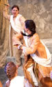 Casca with knife upraised is behind Caesar who is turning and ready to hit Casca with an elbow as two other conspirators in front move in. A curtain around a column and a mottled background are behind. 