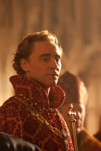 Henry V in regal cloak of red and gold, with a necklace around his neck and a bishop in the background