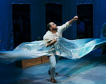 Pericles strides into a blue sheet wrapping about him as he reaches up with his left hand