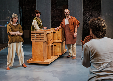 Pericles, with his pack to us at the right, pleads with the three fishermen in rustic wear and standing next to a platform of stacked crates. 