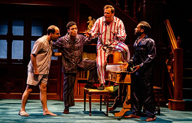 Production photo of Berowne standing on a library study table as the other lords gather around.