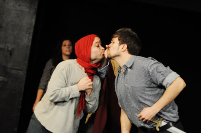 thisbe in red scarf over his head puckers up as he seems to kiss Bottom between the "chink" (two spread fingers) in the wall