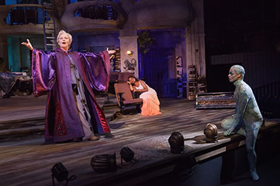 Production photo of Prospera speaking, Mirnada sleeping, and Ariel leaning on the stage listening