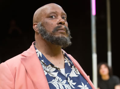 Thomas as Falstaff wearing pink jacket over flowered blue shirt, a full beard and bald head