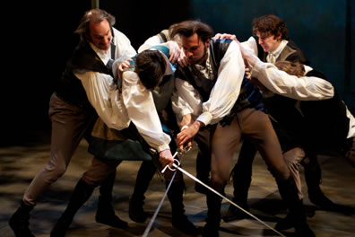 Two men cross swords close together as four others reach to their shoulders trying to pull them apart.