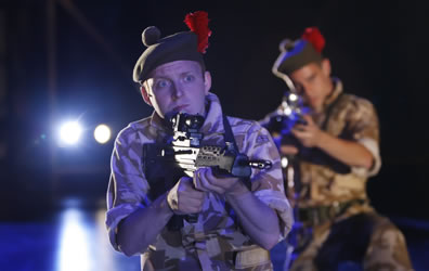 Scottish solders with the red plumes in their berets kneel with rifles poised and what looks like car headlights shining from the back