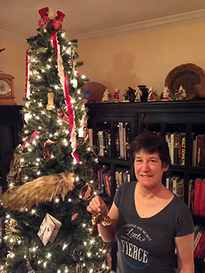 Sarah in t-shirt saying "Though she be but little, she is fierce" holding a glass ornament of a tiger to put on the Shakespeare-History Christmas tree in our library.