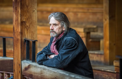 Jeremy Irons leaning with arms crossed on a balcony railing in a rustic theater