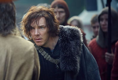 Richard in shaggy hair, a chain pendant draped over his blue shirt, and a fur-line cloak hunches over as he stairs at somebody with an army behind him.