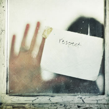 A fuzzy image of a woman through a window holding a sign up against the pane saying "respect"