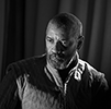 Denzel Washington as Macbeth looking contemplative in royal robe with curtained background (black and white photograph).