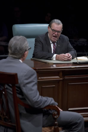 Johnson sitting in a blue-backed chair at his wood desk, hands folded on the desk, speaks to slumping Wilbur Mills in chair, back to us.