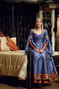 Alais in a rich blue gown sits on the end of a bed in The Lion in Winter