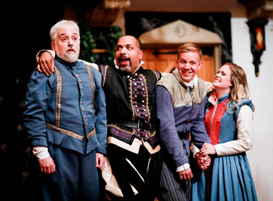 Leonato in blue renaissance uniform jacket and pants with gold trim, Don Pedro with his arms around everybody and wearing black and purple renaissance short jacket and breeches, Claudio laughing and wearing a purple jacket, striped pants and black belt with tan shoulder shawl, and Hero holding his hand and wearing a blue dress with red trim on the front and white shirt.