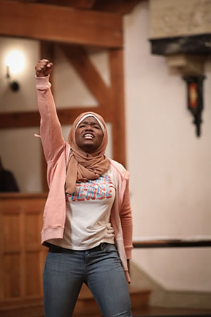 Production photo of Aaliyah in jeans, t-shirt, and Hijab with fist upraised