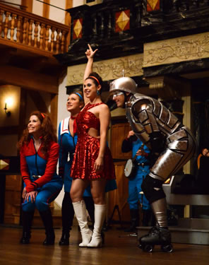 Miranda in a metalic red dress and white go-go boots with arm upraised, Gloria in red and aqua flight suit crouched down, Glenzer bent over, and robot-dressed Arial bend over, too.