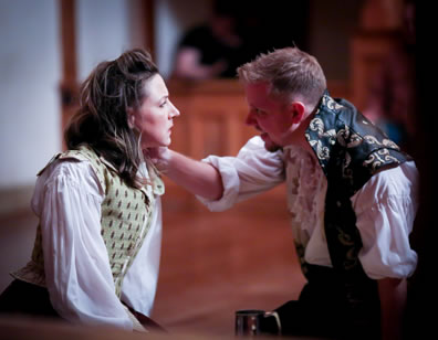 Sitting on the stage, Burbage in floral vest, unbuttonned over puffy white shirt, faces Judith with his hand on her left shoulder, she dressed in simple Elizabethan waistcoat and dress.