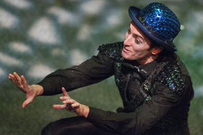 Puck wearing his blue sequined bowler and green sequined vest squats with his hands expressively held out before him, and you can see the dappled light on the stage.
