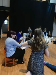 Diana Green sitting on a tiny child's chair gives instruction to kids sitting on the floor around her