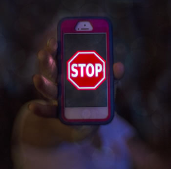 A hand holding to the camera a smartphone with a stop sign on the screen--looks graphic cartoon like