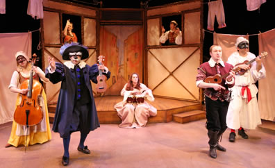 On the stage, Rosetta in yellow maids dress with apron and brown mask plays cello, Il Dottore in purple renaissance type gown with white coller and feather cap but bushy eyebrow and mustache mask holds the ukelel, Celia sitting on the platform in her dress plays bongos, Orazio in a red jerkin and black trowsers with boots plays a ukelele, Pulcinella in white clown outfit with red sash and white cone cap plus black mask plays ukele, Isabella holds up two fingers in the window at the back, and Luzio holds up both hands in the other window