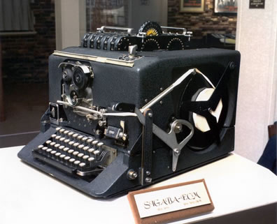 What looks like a big, boxy typewriter, with a computer tape spindel on the visibal side, and contraptions sticking out of the top, including disks