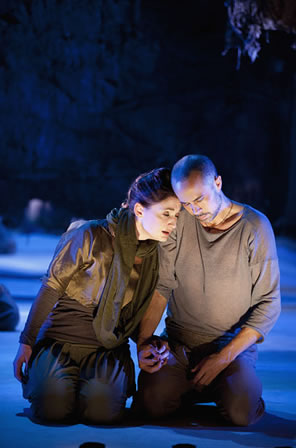 Actors kneel on the stage, holding hands, heads bowed into each other.