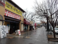 Business district street, rain soaked sidewalk, and matress store to front left, with "Big Sale" board in front and matress leaning against wall
