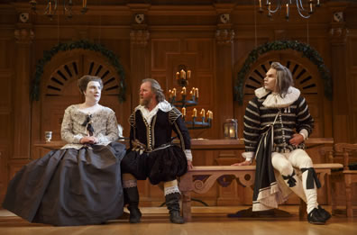 Sitting on a bench in front of a table, Maria in silver blouse and gray skirt, Toby in black Elizabethan outfit, and flaxen haired Aguecheek in a black and white striped top, white pants with black ribbon garters at the knees, and a huge coller ruff