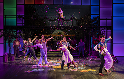 Dancers line up diagnally across stage at the end of their dance, a partner hanging on the arm of the other. Psychedelic lights on the floor, confetti falling, Hyman playing guitar on the gangway above.