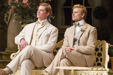 Jack and Algernon sit in nearly identical cream-colored three-piece suits with bowties and stiff collars, legs crossed, on a garden bench.