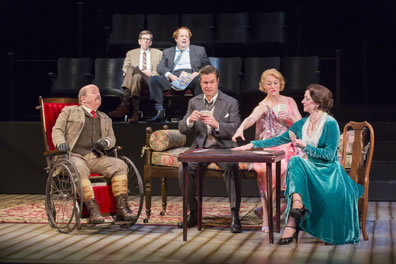 With Moon and Birdboot sitting in theater seats in the background, watching, Major Magnus dressed in brown hunters outfit, Simon Gascoyne in suit and vest, Felicity Cunningham in pink patterned flighty dress, and Cynthia Muldoon in richly turgouis dress, legs crossed, play cards at a table. 