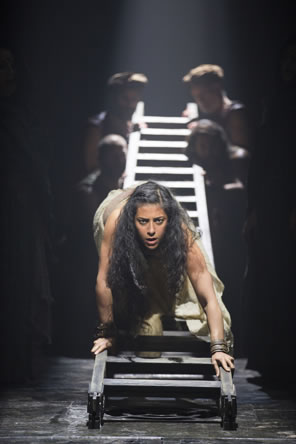 Salome climbs headfirst down a ladder held up by an ensemble of actors at the other end.