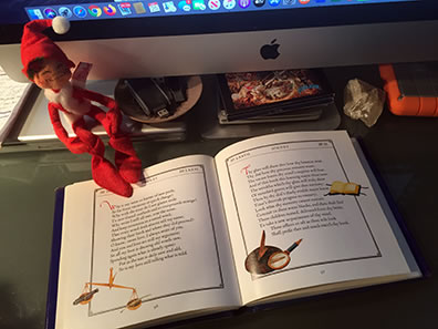 The illustrated book of Shakespeare sonnets opened to Sonnet 77, with an Anna Lee elf sitting on it, the bottom edge of desktop iMac in the background.