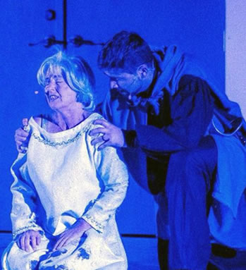 Production photo of Lear sitting with Kent leaning over from behind, hands on her shoulders