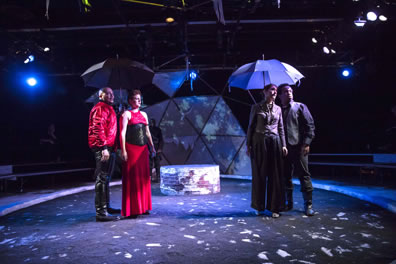 Cornwall in red jacket and black leather pants and Goneril in red dress with black bustier stand under one umbrella; Goneril in purple gray short jacket and blousy pants and Oswald in dark pants and shirt and gray vest stand under the other umbrella.